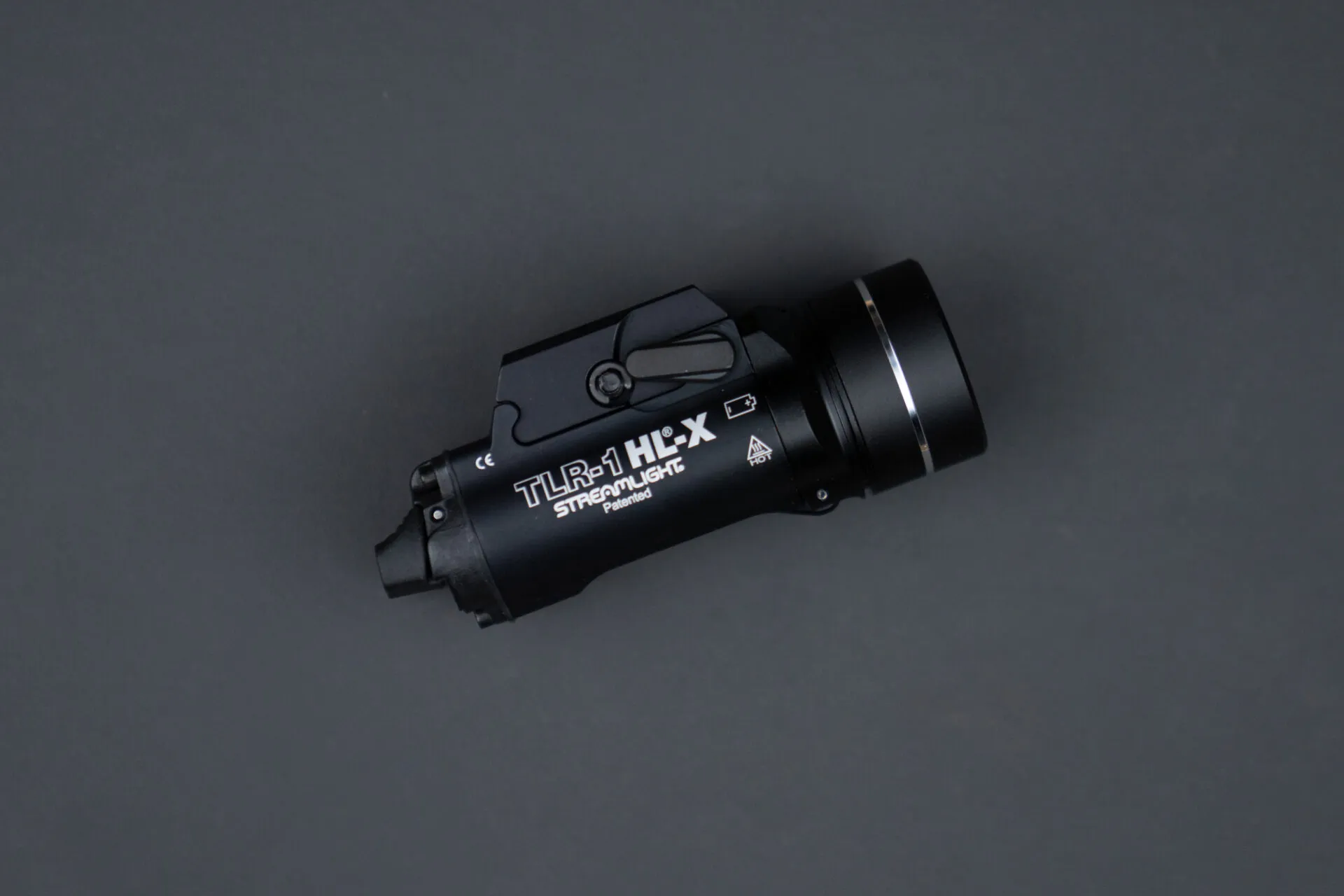 Top-down view of a black Streamlight TLR-1 HL-X high-output tactical weapon light, centered on a matte gray background. The hard-anodized aluminum body displays crisp white laser engravings reading "TLR-1 HL-X" and "STREAMLIGHT Patented," highlighting the rail mounting clamp mechanism, temporary toggle switch, and a silver ring accent near the front bezel lens.